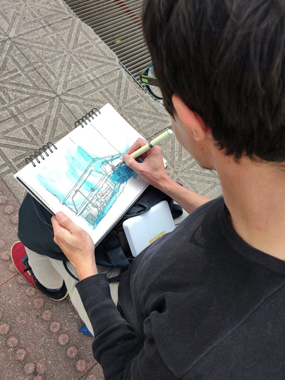 Foto: Ivan Jerônimo sentado desenha com o caderno no colo