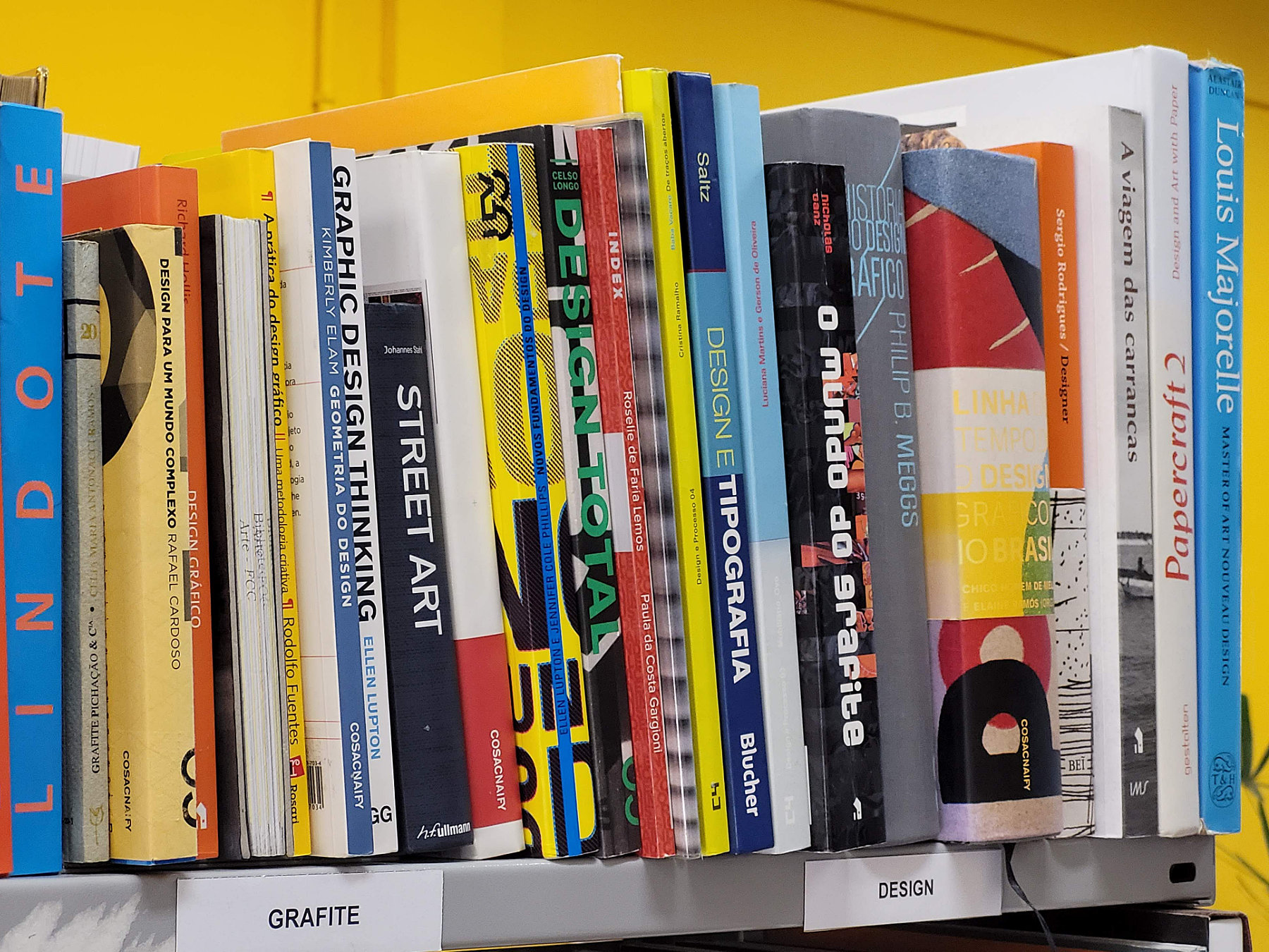 Foto de livros de design e de grafite organizados no andar de uma estante