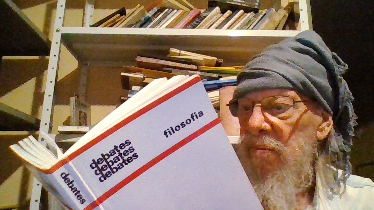 Escritor, artista e crítico Jayro Schmidt lê o livro “Debates - Filosofia” em sua biblioteca