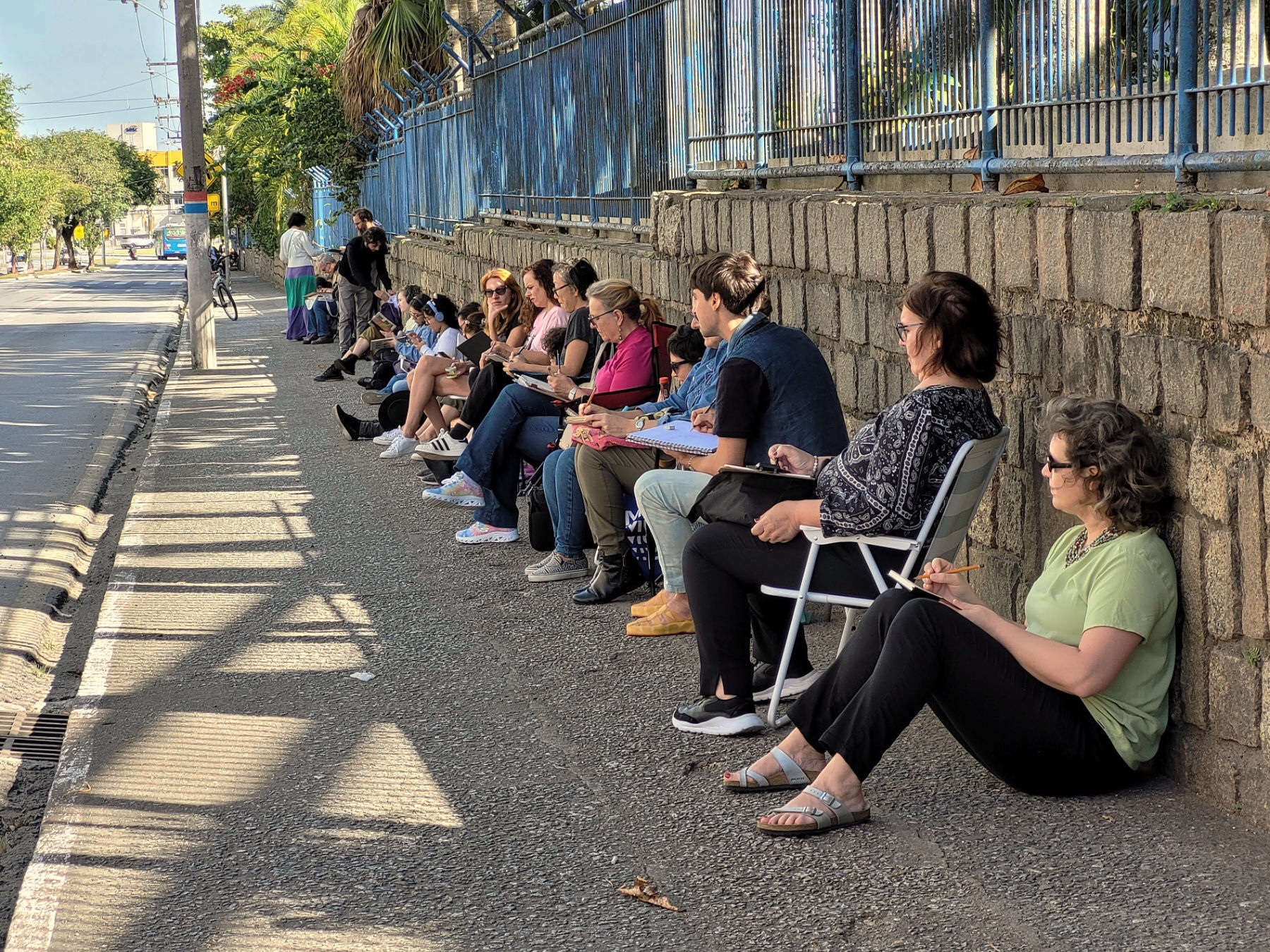 Calçada na avenida Mauro Ramos, em frente ao Instituto, com cerca de vinte participantes sentados, enfileirados, desenhando
