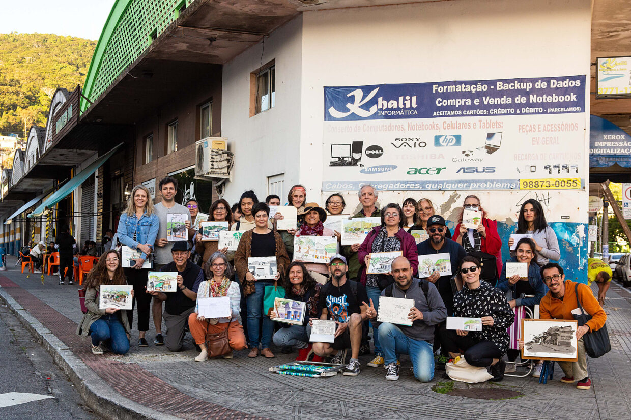 Foto com cerca de 30 participantes do Urban Sketchers Florianópolis em frente a uma das esquinas do prédio da antiga rodoviária em um fim de tarde