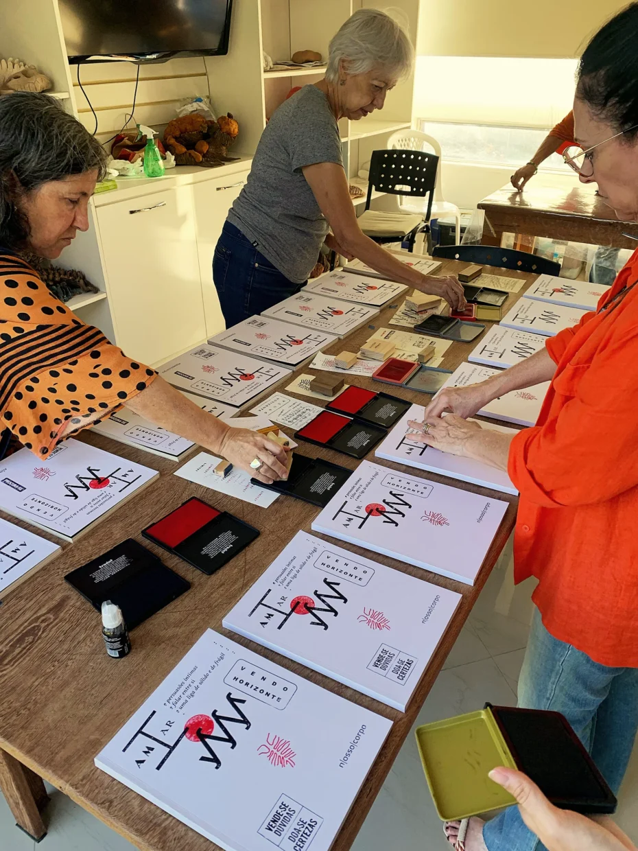 Foto mostrando pessoas ao redor de uma mesa, carimbando as capas dos livros que estão sobre ela