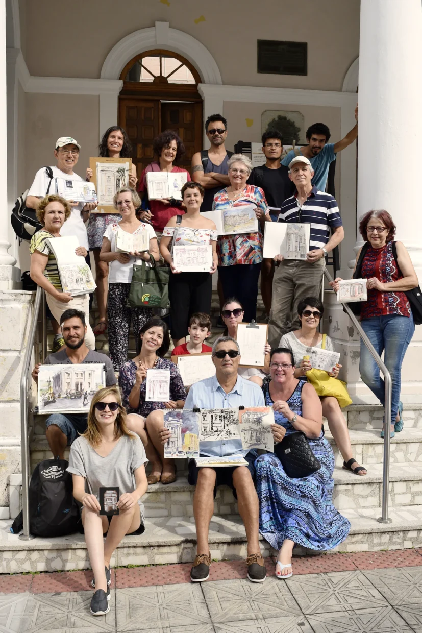 Foto com os participantes do encontro do urban sketchers sentados na escadaria do museu, segurando seus desenhos